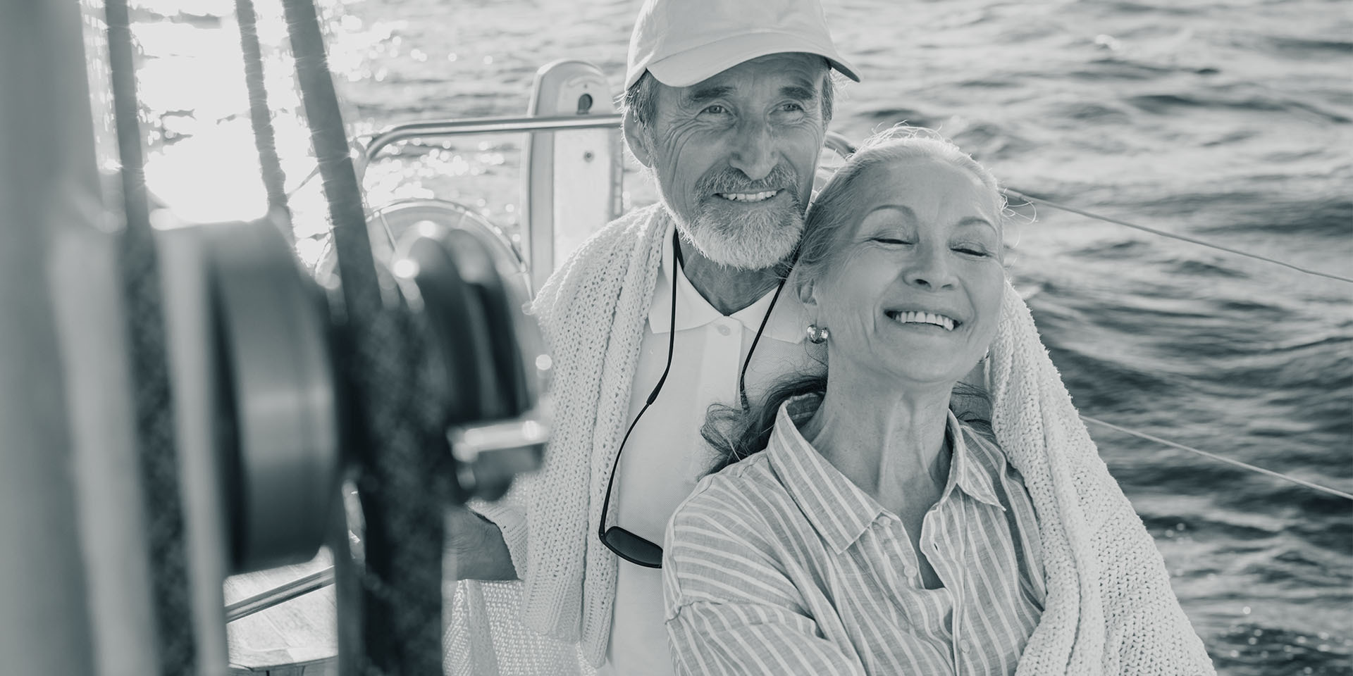An older couple sitting on a sailboat, laughing and enjoying the trip out at sea.